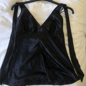 Jättefint silkessaktigt svart linne - Svart halterneck linne. Linnet är i ett glansigt material lite silkesaktigt med är väldigt bekvämt. Linnet har en dragkedja på ena sidan och band som knyts i nacken! 