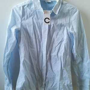 Skjorta  - Ljusblå med vita ränder. Aldrig använd. Lappar kvar. Storlek 34 