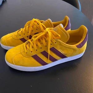 Adidas Sneakers Stl 40 - Säljer mina Adidas Gazelle sneakers som jag bara använt en gång. De är mörkgula med vinröda/lila detaljer. 