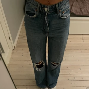 Jeans från Gina i strl 34 - Jeans från Gina tricot i en mellanblå färg. Jeansen har hål på knäna och de är i gott sick. Hör av er vid frågor! Storlek 34