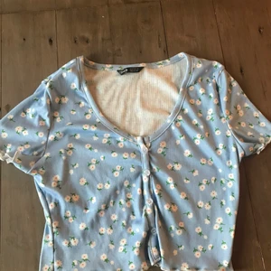 Blå blommig tröja  - En blå tröja med vita blommor på och knappar längst magen . Köparen står för frakten 