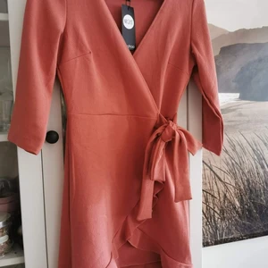 Klänning - Puderrosa/dusty pink klänning med volang i strl 36  från boohoo. Liten i strl Aldrig använd, så nyskick. Omlott med ihoppsydd o knytband i midjan Ny med lapp!  🌸 🌱