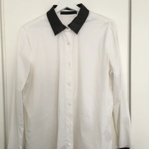 Skjorta - Vit bomullsskjorta med svarta lammskinnsdetaljer kring kragen och ärmar. Använd fåtal gånger, i mycket gott skick. Storlek EU 38  Nypris: 2300 SEK