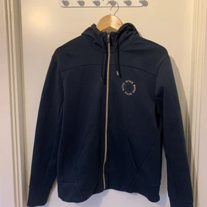 Mörkblå Hugo Boss Hoodie med dragkedja i storlek M - Marinblå Hugo Boos hoodie med guld/brons färgad dragkedja. Använd en del, däremot inga skador eller fläckar men små ”nopprar” på tyget finns. Går att få bort dock. Passar storlek M, Inge mer eller mindre. Bekvämt material invändigt. Nypris ungefär 1500kr.