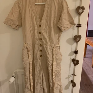 Beige jumpsuit - Beige jumpsuit från Ginatricot. Köpt för något år sen för cirka 600kr. Två fickor och ett midjeband för att definiera figuren/anpassa storlek. Behövs strykas lol