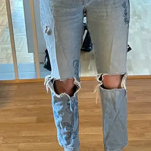 Väldigt snygga ljusblåa högmidjade jeans i mycket bra skick med stora hål på knäna, plus ett litet hål längre upp på benet och ett hål i högra backfickan. Jeansen har jättefina blåa broderade blom- och växt detaljer på båda benen :) Köpta på H&M och är storlek 36 men skulle säga att de passar mycket bra på 38:or också eftersom de är ganska stora i midjan🙂 Kontakta för fler bilder, frågor eller vid intresse!😊 Frakt tillkommer!!