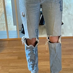 Ljusblåa högmidjade jeans med hål och blomdetaljer - Väldigt snygga ljusblåa högmidjade jeans i mycket bra skick med stora hål på knäna, plus ett litet hål längre upp på benet och ett hål i högra backfickan. Jeansen har jättefina blåa broderade blom- och växt detaljer på båda benen :) Köpta på H&M och är storlek 36 men skulle säga att de passar mycket bra på 38:or också eftersom de är ganska stora i midjan🙂 Kontakta för fler bilder, frågor eller vid intresse!😊 Frakt tillkommer!!