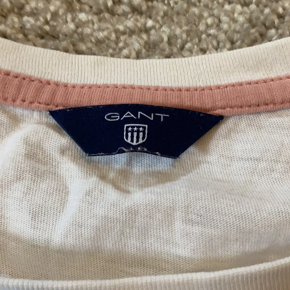 En Gant tröja som är vit med mörkblåa och rosa detaljer.Det finns en lite fläck på tröjan men det är inget som syns så mycket.. T-shirts.
