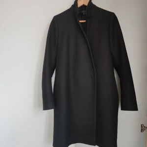 Svart kappa Cos  - Snygg och bekväm kappa till våren! Storlek: 36. Material: Ull, polyamid, kashmir. Nypris ca 2000kr. Använd någon höst och vår, därav tyvärr någon centimeter hål i fodret under båda armarna (endast fodret på insidan och därav inget som märks). Lite nopprig på kragen men inte heller så märkbart. Säljer pga. vuxit ur. Buda från 400 😊 Köpare står för frakt. 