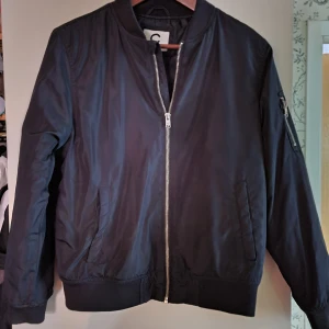 Svart Bomberjacka , Cubus,  strl 164, ( som xs ) - Sparsamt använd,  svart bomberjacka,   innerficka , ficka med blixtlås på höger arm , samt två framfickor.  Silverfärgade blixtlås. Mycket fint skick!   Leveranskostnaden står köparen för. 