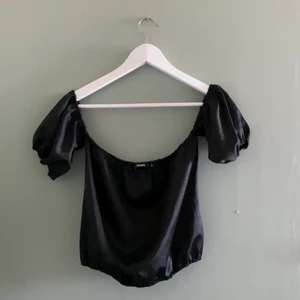 Off-shoulder topp  - En svart off-shoulder topp i satin material. Puffärmar som är fastsydda i toppen. Använd ett fåtal gånger och köpt på BikBok. 