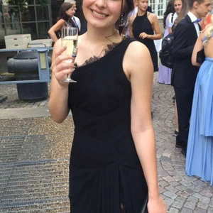 Svart Balklänning  - Svart balklänning med mycket fina detaljer i tyget och med spets. Det finns en slits i kjolen med spets omkring. Klänningen slutar precis vid marken om man är 165cm lång och har ca 10 cm höga klackar. Slitage i nederkanten av kjolen (kanten mot marken). I övrigt i mycket bra skick, använd fåtal gånger. Klänningen är skräddarsydd och kostade 5000kr då jag köpte den. 