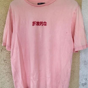 Rosa T-shirt med tryck  - T-shirt från Urban Outfitters med rött tryck på ryggen och broderad text på framsidan. Det är ett litet hål på framsidan precis vid armhålan, men det går lätt att sy igen.   Tröjan är i storlek M men passar både på S och L beroende på hur man vill att den ska sitta.