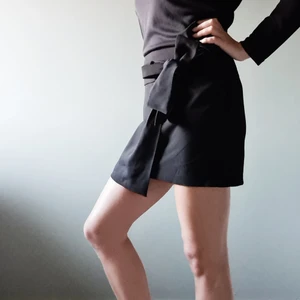 Svart omlottkjol med rosett  - Kort svart omlottkjol med rosett, använd ett fåtal ggr. Storlek 38. Nyskick.