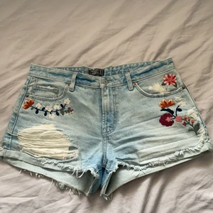Abercrombie&fitch shorts - Supersnygga och somriga shorts med slitningar och broderade blommor från Abercrombie&Fitch. W31. Slitningar på fickor både fram och baktill. Väl använda men felfria. Köpta i Paris för flera år sen i A&F butiken så tvivlar på att dom finns kvar. Köparen står för frakt och betalas via Swish✨