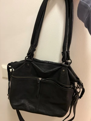 Svart handväska från legend, äkta läder!  - Snygg svart handväska i äkta läder från legend, med dubbla axelband och avtagbar axelrem. Väskan har en stor ytterficka med dragkedja framtill och stilrena metalldetaljer. Perfekt storlek för att få plats med allt du behöver och passar till många olika outfits.