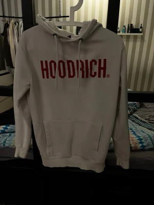 Hoodrich tröja - Snygg vit hoodie från Hoodrich i storlek XS med röd logga framtill. Klassisk modell med huva, dragsnören och känguruficka. Perfekt för en chill och trendig streetwear-look.