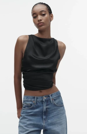 Svart omlott topp med rosett - Snygg svart omlott topp i satin med öppen rygg och stor rosett bak. Croppad passform och ärmlös design som ger en cool och elegant look. Perfekt att matcha med jeans eller kjol för en trendig stil.