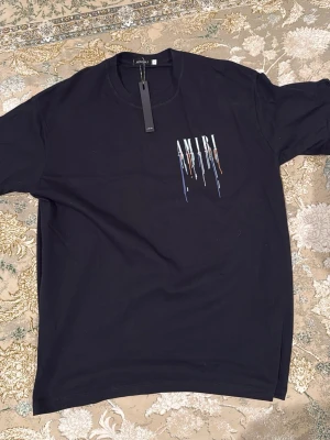 Svart AMIRI t-shirt med tryck - Svart t-shirt från AMIRI med färgstarkt tryck och droppande effekt på bröstet. Klassisk rund halsringning och korta ärmar. Perfekt för dig som vill ha en stilren men ändå unik look.