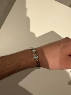 Silverfärgat armband med droppformade stenar - Snyggt armband i silverfärg med flera stora, droppformade glittrande stenar. Länkarna är smala och armbandet har en elegant design som sticker ut. Perfekt för dig som gillar att glänsa lite extra.