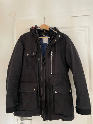 J.LINDEBERG jacka  - Säljer en fin jacka från J.LINDEBERG, stil ren och väldigt populär lite längre jacka perfekt till vintern/våren. Avtagbar luva och avtagbar dunväst inuti jackan. Lite militär stuk. Storlek medium herr. Saknar tyvärr vissa knappar vid höften