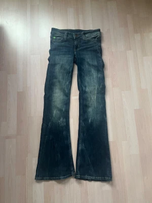 Mörkblå bootcut jeans från Cheap Monday - Säljer ett par mörkblå bootcut jeans från Miss Sixty med slitna detaljer och lätt tvättade partier. Jeansen har klassisk femficksmodell, låg midja och grönt Miss Sixty-märke bak i linningen. Tillverkade i bomull med en cool vintagekänsla. Har aldrig använt jeansen. 