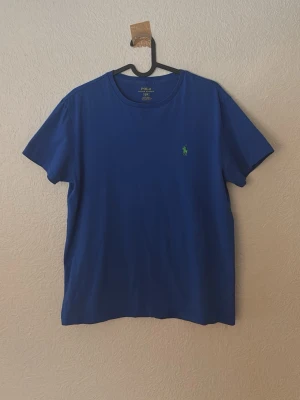 Blå t-shirt från Polo Ralph Lauren - Snygg blå t-shirt från Polo Ralph Lauren med klassisk grön broderad logga på bröstet. T-shirten har rund halsringning och korta ärmar. Tillverkad i mjuk bomull för en skön känsla och enkel stil.