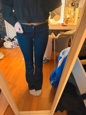 Bootcut jeans med låg midja  - Säljer ett par mörkblå bootcut jeans med klassisk femficksdesign och låg midja. Jeansen har en snygg, smal passform upptill och lätt utsvängda ben. Storlek 34.