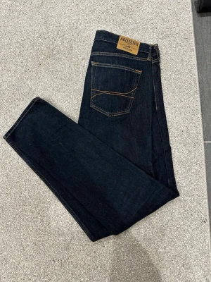 Mörkblå jeans från Hollister - Snygga mörkblå jeans från Hollister med klassisk femficksdesign och kontrastsömmar. Jeansen har en rak passform och är tillverkade i ett mjukt denimtyg som sitter skönt hela dagen. W34 och L34.Perfekta för dig som gillar en stilren och tidlös look. Skriv över det minsta lilla eller över den minsta funderingen!🔥🔥