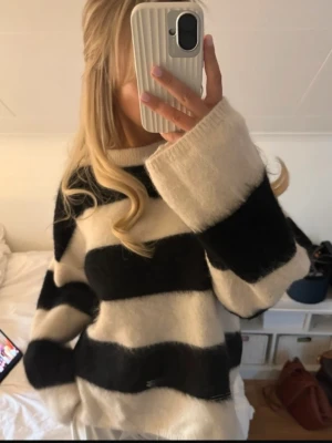 Randig oversized stickad tröja från HM mohair - HM mohair! Säljer en oversized stickad tröja med breda svarta och vita ränder. Tröjan har långa ärmar och en lös passform med nedhasade axlar. Materialet ser fluffigt och mjukt ut, perfekt för kalla dagar. Inga synliga loggor eller märken.