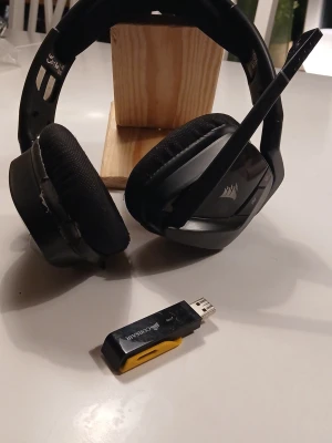 Corsair trådlöst gamingheadset svart - Säljer ett svart trådlöst gamingheadset från Corsair med inbyggd mikrofon och mjuka öronkuddar i tyg. Headsetet har en robust plastbåge och medföljer gör en USB-dongel för trådlös anslutning. Perfekt för gaming och voicechatt.Det är lite trasiga på några ställen so m trasikt på ringen 