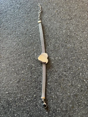 Silverfärgat armband med hjärta - Snyggt armband i silverfärg med en tunn kedja och ett stilrent hjärta i mitten. Justerbar längd med kedja och karbinlås. Perfekt accessoar för att lyfta din outfit med en enkel men elegant detalj.