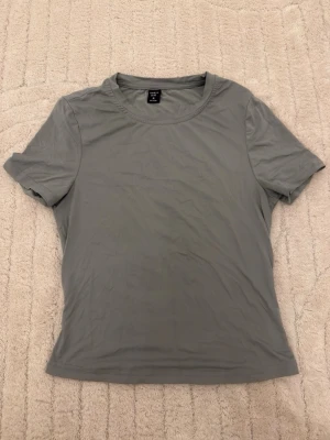 Grå basic t-shirt - En enkel och stilren grå t-shirt från med rund hals och korta ärmar. Perfekt för dig som gillar minimalistisk stil och vill ha ett plagg som funkar till många outfits. Materialet känns mjukt och lätt mot huden.
