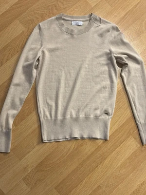 Beige stickad tröja Holly & Whyte - Snygg beige stickad tröja från Holly & Whyte by Lindex. Tröjan har rund halsringning, långa ärmar och ribbade muddar vid ärmslut och nederkant. Perfekt basplagg i garderoben och lätt att matcha till olika outfits.