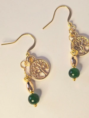 Guldörhängen med träd och gröna pärlor - Unika örhängen i guldfärgad metall med ett detaljerat livets träd-hänge och dekorativa gröna pärlor. Örhängena har även en oval guldfärgad detalj ovanför pärlan. Perfekt för dig som gillar naturinspirerade accessoarer.
