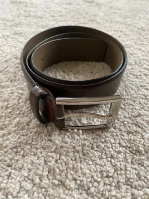 Hugo boss bälte - Snyggt brunt skärp från Hugo i äkta skinn med silverfärgat spänne. Storleken är 100cm.  Hör av er vid frågor!