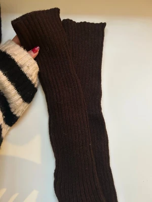 Bruna stickade pulsvärmare / benvärmare - Mörkbruna, ribbstickade pulsvärmare/ benvärmare i ett mjukt och stretchigt material. Perfekta att dra över händerna för extra värme och stil. Långa och smala i modellen, utan tumhål.