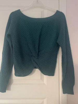 Mörkgrön stickad tröja med twist - Mysig mörkgrön stickad tröja med lång ärm och twistad detalj framtill. Tröjan har en bred rund halsringning och ett diskret strukturmönster i stickningen. Perfekt för lager-på-lager och chill dagar.