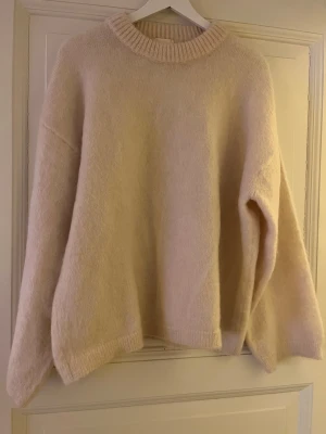 Ljusbeige mohairmix tröja från H&M  - Mysig ljusbeige stickad tröja från H&M i en mjuk mohair- och ullblandning. Tröjan har avslappnad passform, rund halsringning och ribbade muddar vid hals, ärmslut och nederkant. Perfekt för lager på lager under kyliga dagar.