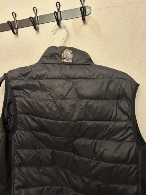 Svart dunväst från Parajumpers - Snygg svart dunväst från Parajumpers med lätt och smidig design. Västen har quiltad struktur och hög krage med broderad logotyp på baksidan. Perfekt för lager-på-lager och enkel att bära tack vare super lightweight-materialet. Kedjan i mitten e en bit som åkt av och den gula vid halsen e borta då den blev klippt i skolan av några killar jag bråka med