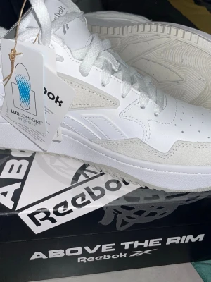 Vita Reebok sneakers med mockadetaljer - Snygga vita sneakers från Reebok med klassisk låg siluett. Skorna har detaljer i både slätt läder och mocka, samt vita skosnören och en rejäl yttersula. Perfekta för dig som gillar stilrena och tidlösa sneakers med extra komfort tack vare LuxComfort-innersulan.