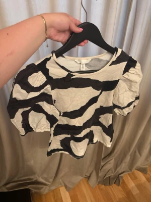 Zebramönstrad croppad topp - Cool croppad topp från H&M med svartvitt zebramönster och puffiga korta ärmar. Perfekt för att lyfta vilken outfit som helst med sin unika stil och trendiga look.