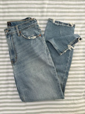 Abercrombie & Fitch ultra high rise mom jeans long length - Jeans från Abercrombie & Fitch i en ljusblå tvätt. Modellen heter ”Ultra High Rise Mom Jean” och har raka ben och obearbetade kanter nedtill. Jeansen har fem fickor och en gylf med dragkedja och knapp. Det här är den långa versionen av jeansen. De framhäver midjan och baken på ett fantastiskt sätt.