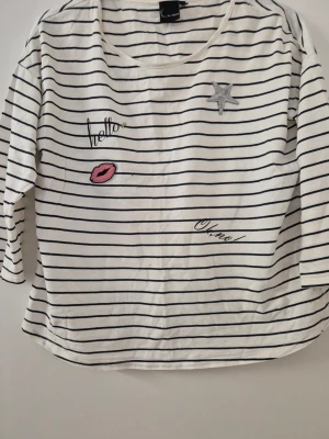 Tröja - Vit tröja med svarta horisontella ränder och broderade detaljer som en silverfärgad stjärna, rosa läppar och texten 'hello' och 'oh no!'. Tröjan har rund hals och trekvartsärmar. Tillverkad i mjuk bomull och har en avslappnad passform.
