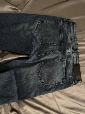 Mörkblå jeans från Dressmann - Snygga mörkblå jeans från Dressmann med klassisk femficksmodell och raka ben. Jeansen har en diskret tvättad look och detaljer i metall vid fickorna. Tillverkade i bomull med en skön passform som funkar till det mesta.