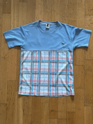  Lacoste t-shirt och shorts - Unik t-shirt från Lacoste med ljusblå ovandel och rutig nederdel i blått, vitt och rött. Matchande shorts. Storlek M passar oxå S. Litet hål i shortsen i båda fickorna. Annars helt felfria! T shirt 500kr, shorts 300kr och båda 700kr.