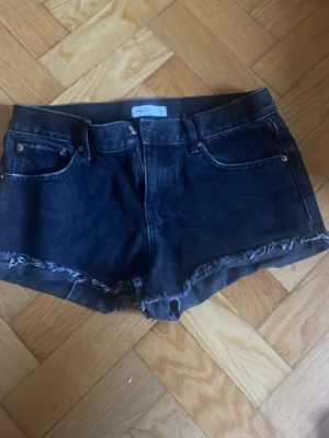 Svarta jeansshorts med fransig kant - Svarta denimshorts från Perfect Jeans med fransig kant och klassisk femficksdesign. Shortsen är i storlek 34 men passar både XS och S