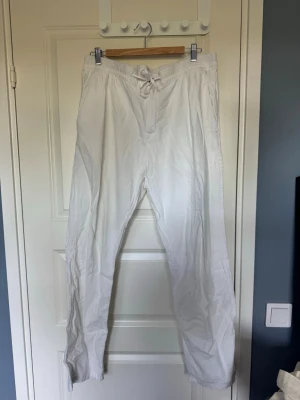 Vita linnebyxor  - Säljer ett par vita linnebyxor med avslappnad passform och snörning i midjan. Byxorna har raka ben och är tillverkade i ett lätt och luftigt linnematerial, perfekta för en chill och stilren look. Har fläckar från en cykelkedja längst ner på höger ben som knappt syns, annars är de i mycket bra skick. 
