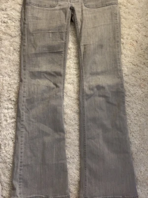 Grå bootcut jeans med fickdetalj - Säljer ett par grå bootcut jeans med snygg fickdetalj och knapp bak. Jeansen har klassisk femficksdesign och är gjorda i mjukt denimtyg. Perfekta för dig som gillar en avslappnad men trendig look . det är en liten fläck på benet som knappt syns 