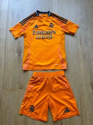 Real Madrid orange matchställ Adidas - Real Madrid orange bortaställ säsongen 2024/25. Storlek 152. 
